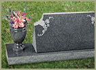 granite monument stone on ground with upright stone with names and dates engraved and granite flower vase on the left with flowers in it